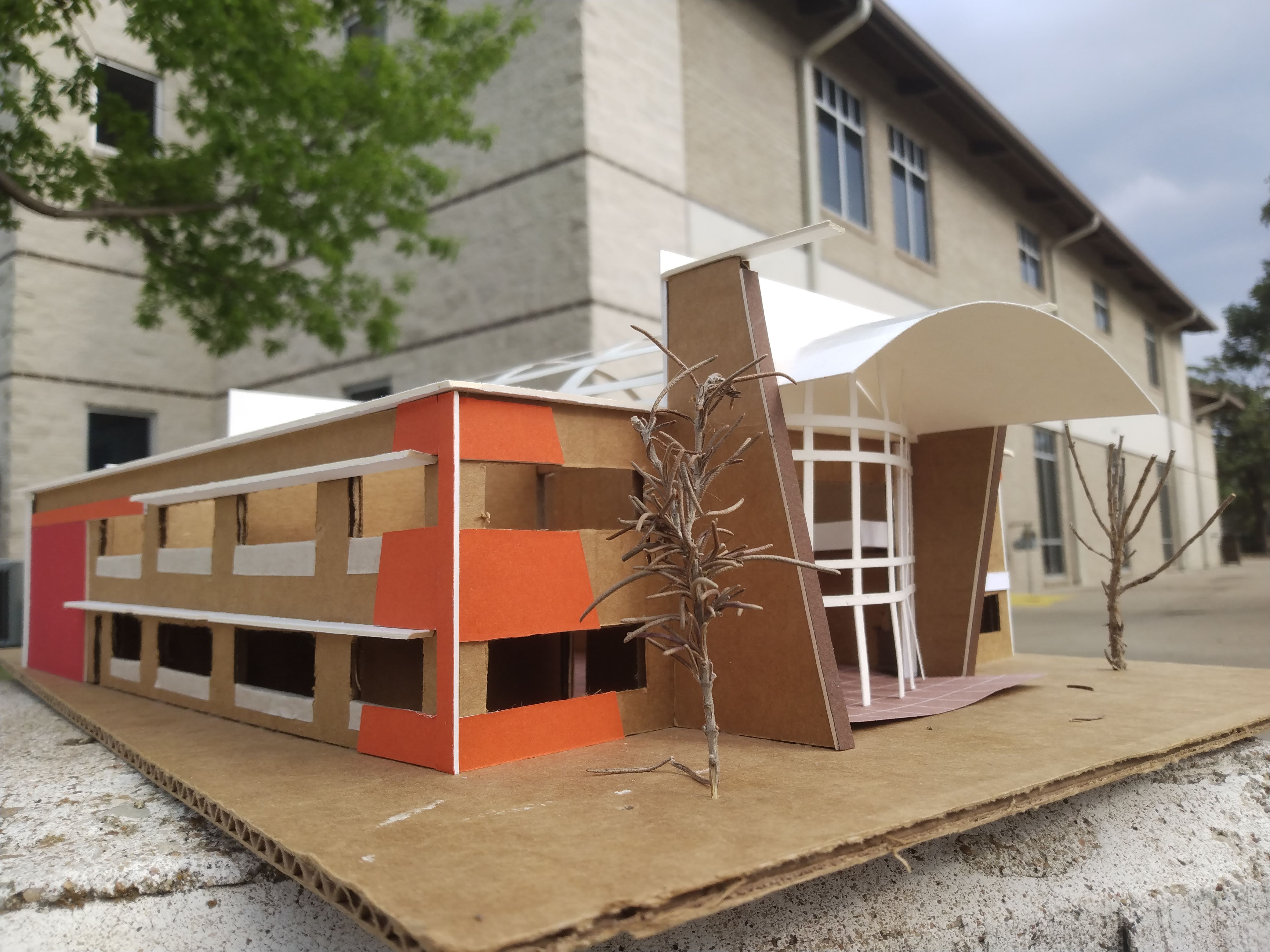 the cardboard model stands on a concrete sidewalk in front of a modern church building blurred in the background